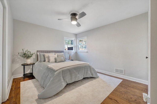 bedroom with ceiling fan, wood finished floors, visible vents, and baseboards