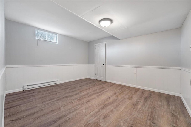 empty room featuring a wainscoted wall, a baseboard heating unit, and wood finished floors