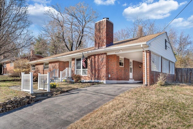 view of front of home with an attached carport, fence, driveway, a chimney, and brick siding