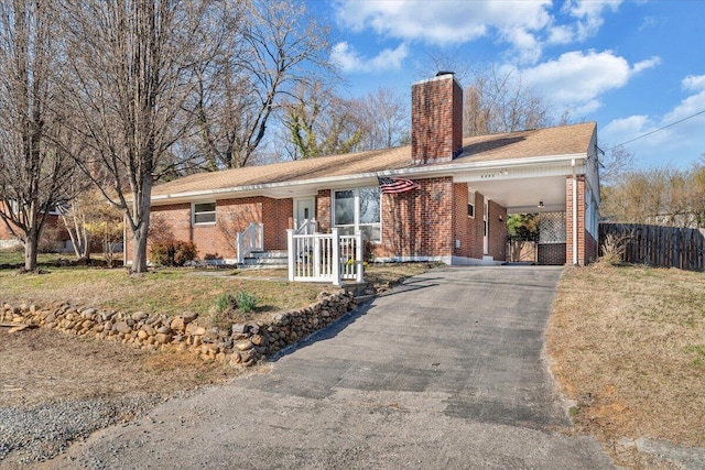 ranch-style home with a front lawn, driveway, fence, brick siding, and a chimney