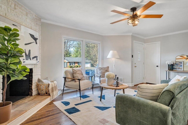 living area with a ceiling fan, wood finished floors, baseboards, ornamental molding, and a large fireplace