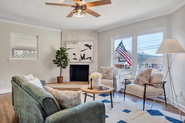 living room with a stone fireplace, wood finished floors, baseboards, and ornamental molding