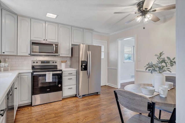 kitchen with backsplash, stainless steel appliances, light wood-type flooring, and ornamental molding