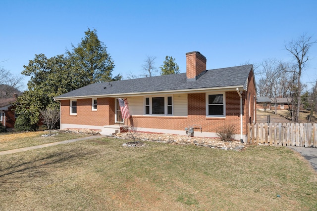 view of front of house featuring brick siding, fence, roof with shingles, a front yard, and a chimney