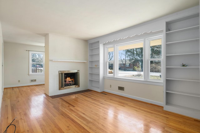 unfurnished living room featuring a fireplace, light wood-type flooring, baseboards, and built in shelves