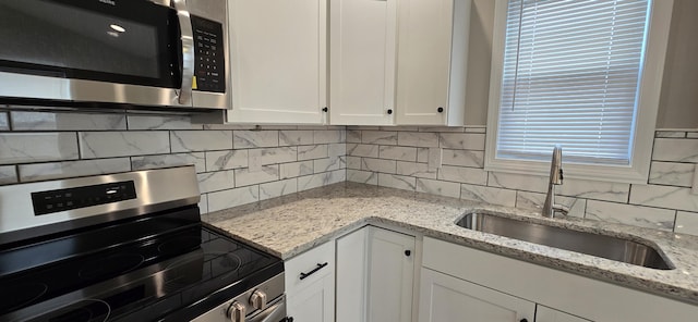 kitchen featuring light stone countertops, a sink, stainless steel appliances, white cabinetry, and tasteful backsplash