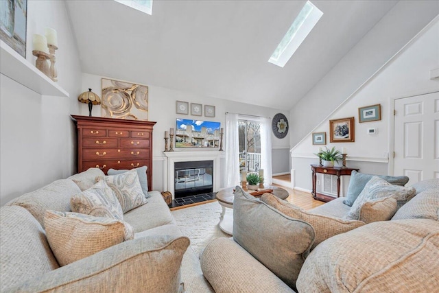 living room featuring vaulted ceiling with skylight, a fireplace with flush hearth, and wood finished floors