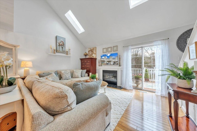 living room featuring a glass covered fireplace, hardwood / wood-style flooring, a skylight, and high vaulted ceiling