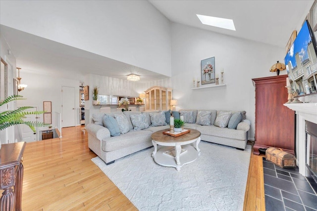 living room with a skylight, a large fireplace, high vaulted ceiling, and wood finished floors