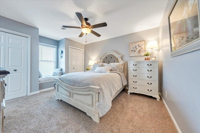 bedroom with light colored carpet, baseboards, two closets, and ceiling fan