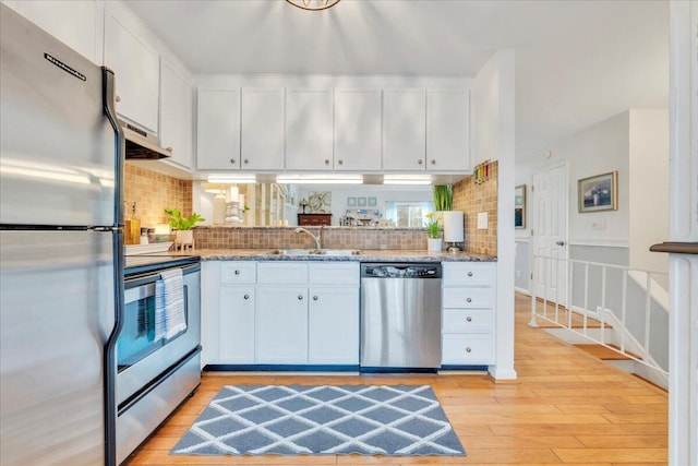 kitchen with light wood finished floors, tasteful backsplash, white cabinets, stainless steel appliances, and a sink