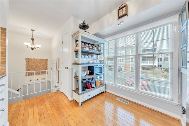 interior space featuring baseboards, visible vents, light wood-style floors, pendant lighting, and a chandelier