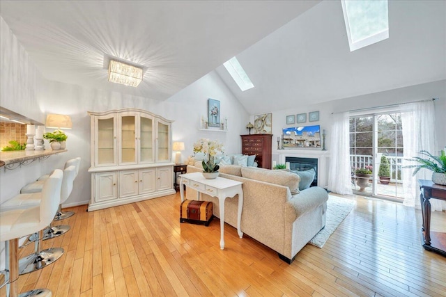 living area with a glass covered fireplace, lofted ceiling with skylight, and light wood finished floors