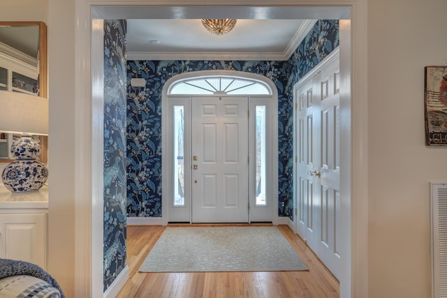 foyer entrance featuring visible vents, ornamental molding, light wood-style floors, wallpapered walls, and baseboards