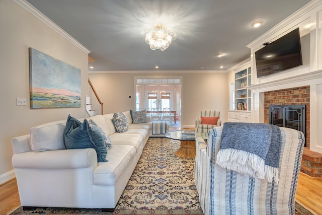 living area featuring a notable chandelier, ornamental molding, a brick fireplace, and wood finished floors