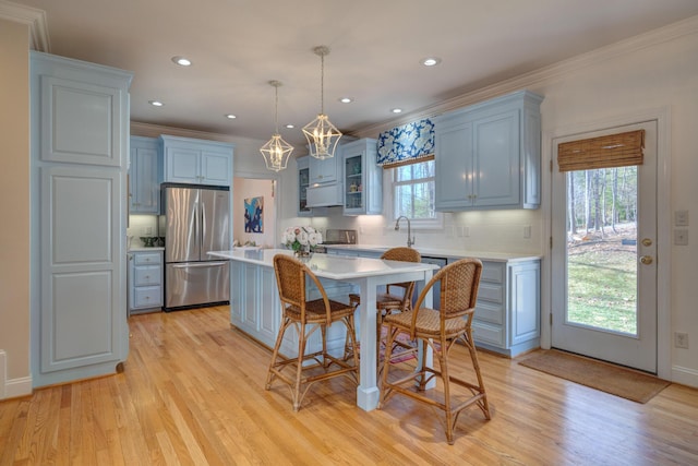 kitchen featuring a kitchen bar, light wood-style flooring, stainless steel refrigerator, a center island, and light countertops