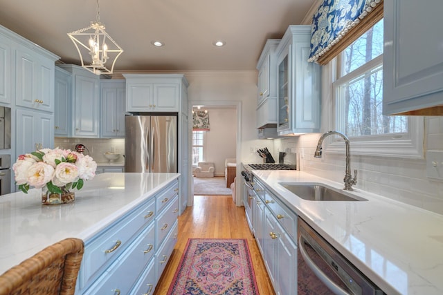 kitchen featuring pendant lighting, light wood-style floors, an inviting chandelier, stainless steel appliances, and a sink