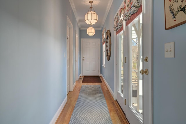 doorway with crown molding, light wood-type flooring, and baseboards