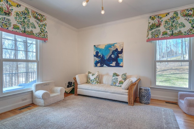 living area with visible vents, wood finished floors, baseboards, and ornamental molding