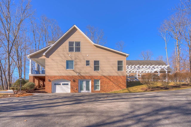 exterior space with a balcony, a garage, french doors, and brick siding