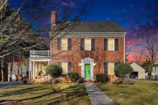 colonial-style house featuring a yard, brick siding, a balcony, and a chimney