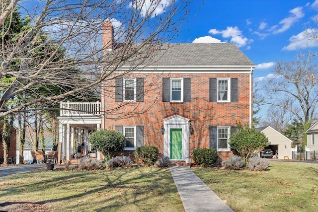 colonial home featuring a front yard, a balcony, brick siding, and a chimney