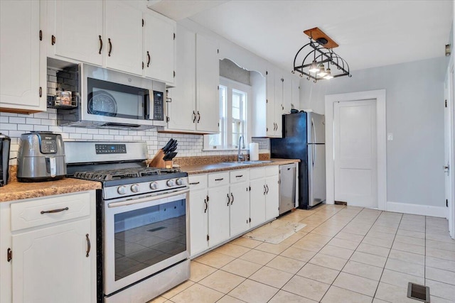 kitchen with a sink, tasteful backsplash, stainless steel appliances, white cabinets, and light tile patterned flooring