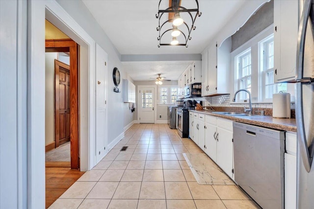 kitchen with ceiling fan, a sink, light tile patterned flooring, stainless steel appliances, and white cabinetry