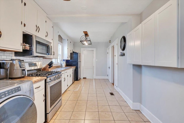 kitchen featuring decorative backsplash, light tile patterned floors, white cabinets, washer / dryer, and stainless steel appliances