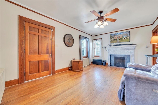 living area with baseboards, light wood-style flooring, a fireplace, and crown molding