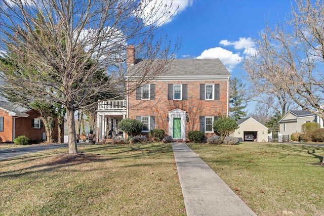 colonial home featuring a front yard, brick siding, a detached garage, and a chimney