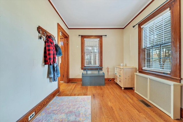 doorway to outside with visible vents, baseboards, light wood finished floors, radiator heating unit, and crown molding