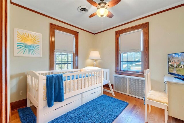 bedroom with crown molding, radiator, wood finished floors, and visible vents