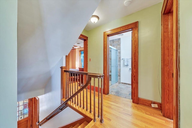 hallway with baseboards, an upstairs landing, and light wood finished floors