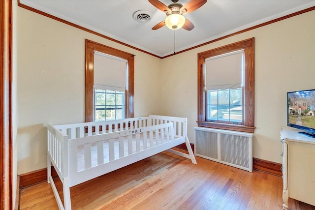 bedroom featuring radiator, wood finished floors, visible vents, baseboards, and crown molding