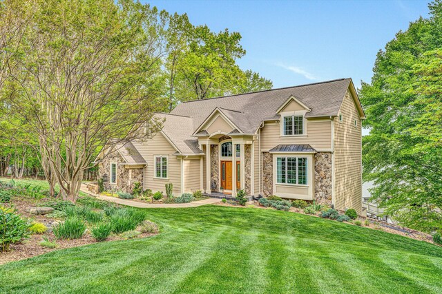 traditional-style home with stone siding, a front lawn, and roof with shingles