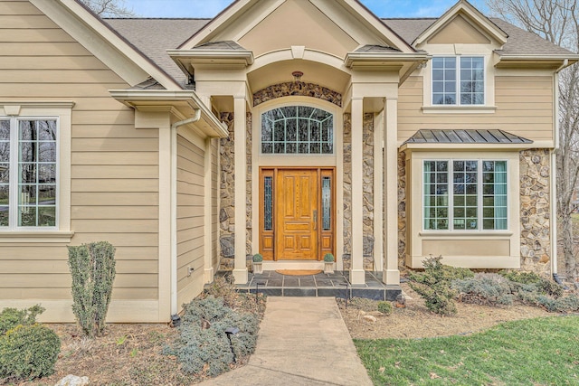 doorway to property featuring stone siding and roof with shingles