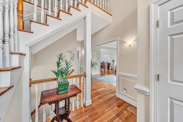 hallway featuring a wainscoted wall, visible vents, a high ceiling, light wood-style floors, and a decorative wall