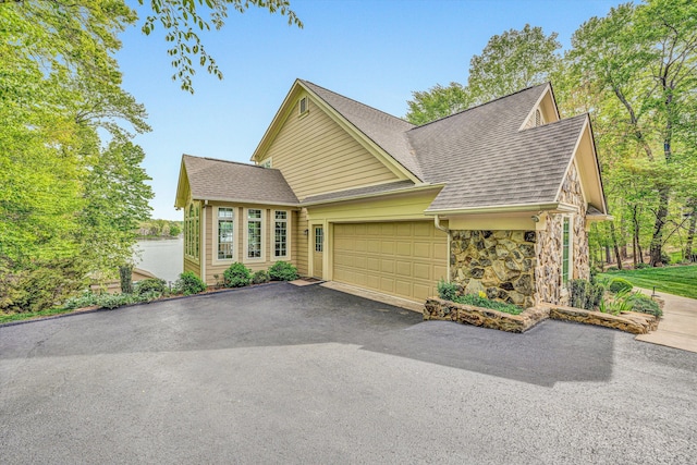 view of front of home with stone siding, an attached garage, a shingled roof, and asphalt driveway
