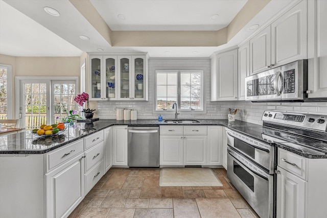 kitchen with backsplash, glass insert cabinets, a peninsula, stainless steel appliances, and a sink