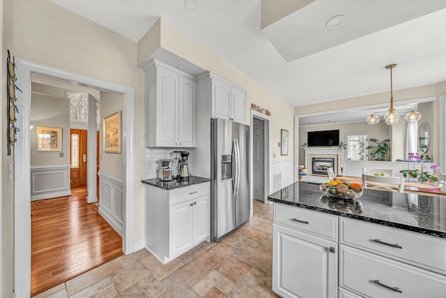 kitchen with dark stone countertops, a glass covered fireplace, stainless steel fridge with ice dispenser, and white cabinetry