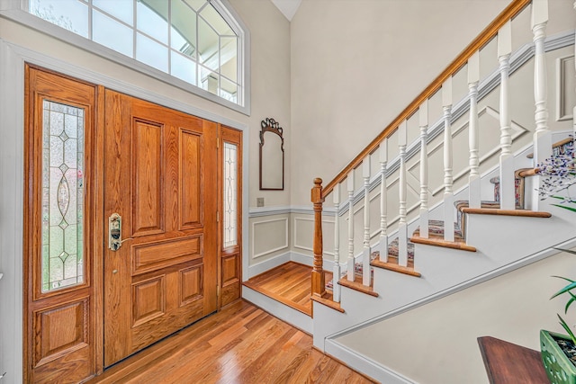 entrance foyer with stairs, light wood-style flooring, wainscoting, a decorative wall, and a towering ceiling