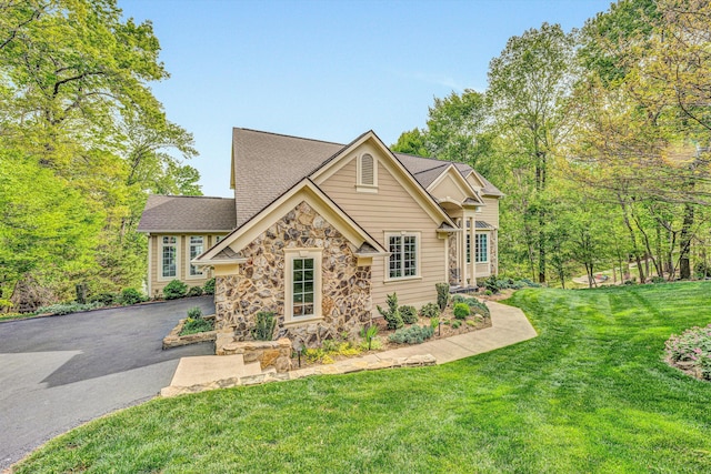 view of front of property with stone siding, a front lawn, roof with shingles, and driveway