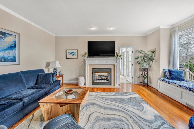 living room featuring a fireplace with flush hearth, wood finished floors, baseboards, and ornamental molding