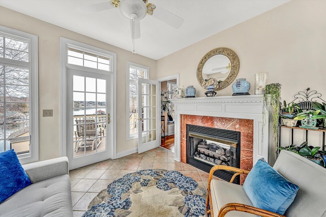 living area with a premium fireplace, a ceiling fan, light tile patterned floors, and baseboards