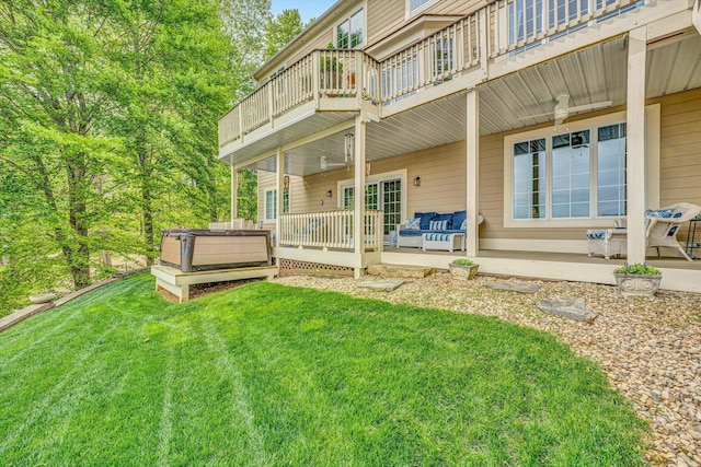 rear view of house featuring a hot tub, a yard, a wooden deck, and a balcony