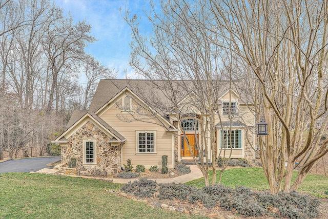 view of front of home featuring a shingled roof, a front lawn, stone siding, and aphalt driveway