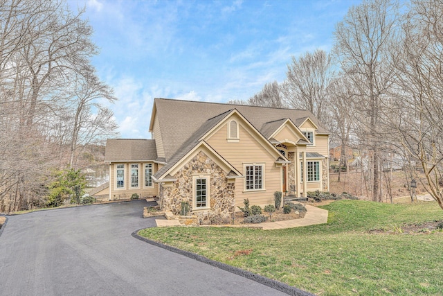 traditional home featuring stone siding, driveway, a front lawn, and roof with shingles