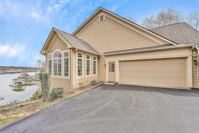 view of front of property featuring driveway, a shingled roof, a garage, and a water view