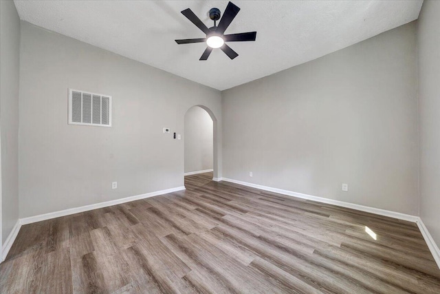 empty room with visible vents, ceiling fan, baseboards, wood finished floors, and arched walkways